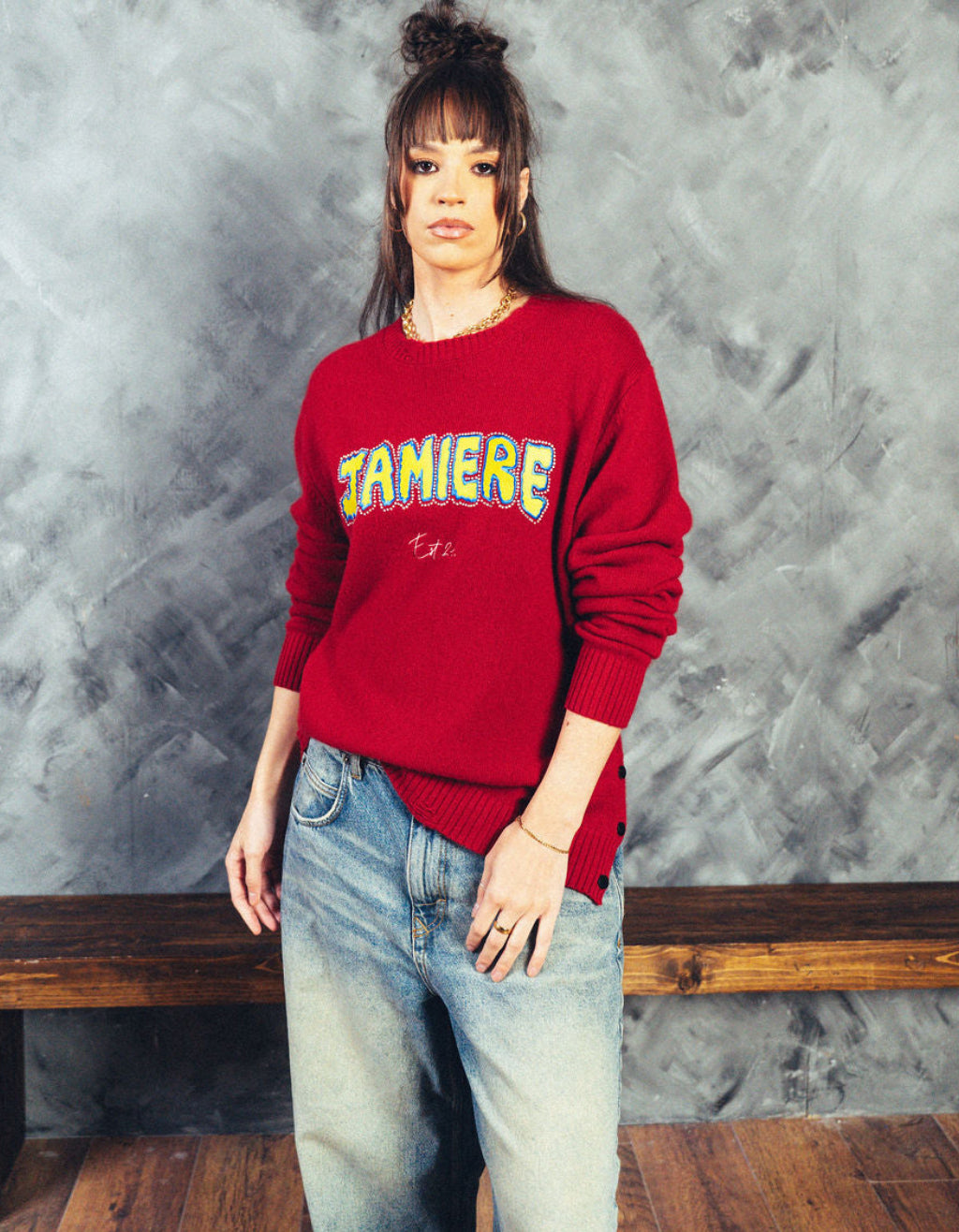 Person wearing a red sweatshirt with text, standing against a textured gray wall.