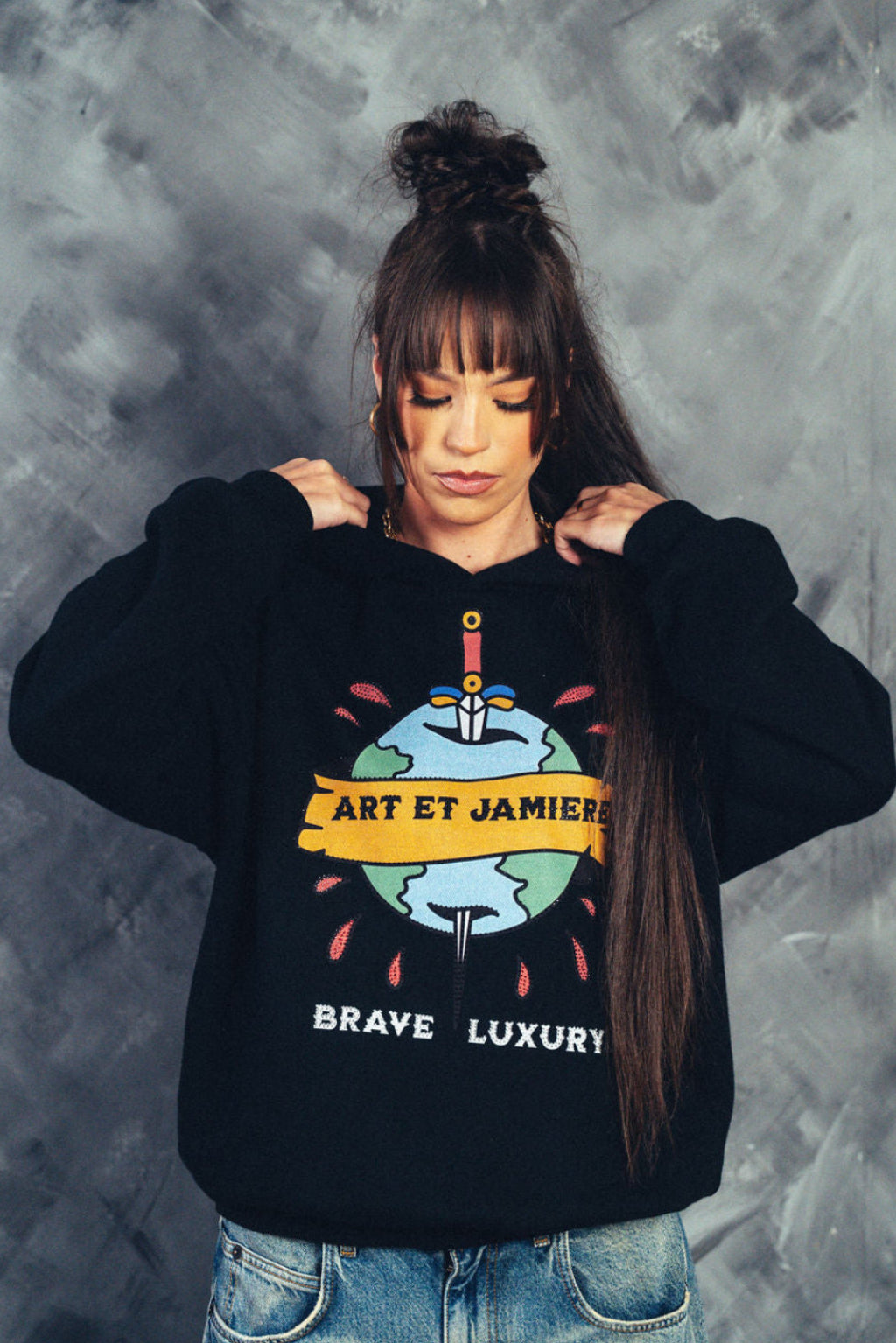Person wearing a black sweatshirt with a graphic design and text, standing against a textured gray background.