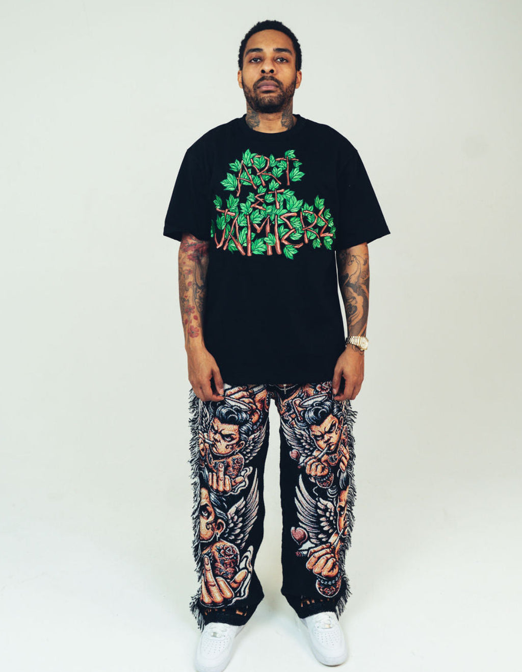 Person wearing a black t-shirt with green graphic design and patterned pants on a white background