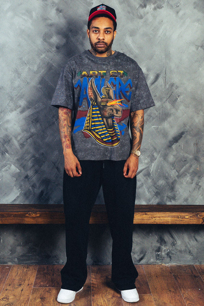 Man wearing a graphic t-shirt standing against a textured gray wall with a wooden bench.